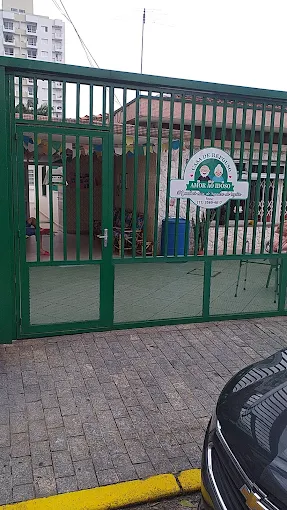 Fachada da Casa de Repouso Amor ao Idoso no Parque Novo Mundo. Portão alto de grade verde com uma placa oval branca com o logotipo e o telefone da instituição. Fachada da Casa de Repouso Amor ao Idoso no Parque Novo Mundo. Portão alto de grade verde com uma placa oval branca com o logotipo e o telefone da instituição.