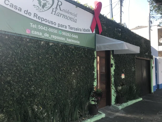 Quarto triplo na casa de repouso com três camas de madeira alinhadas, cobertas com colchas floridas em tons de verde e roxo, armário planejado branco, criado-mudo e quadro decorativo na parede. Quarto triplo na casa de repouso com três camas de madeira alinhadas, cobertas com colchas floridas em tons de verde e roxo, armário planejado branco, criado-mudo e quadro decorativo na parede.