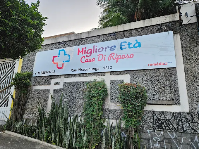 Fachada externa da Migliore Età na Vila Bertioga. Entrada protegida com portões seguros, identificação nítida da instituição e estrutura acessível para a recepção das famílias.